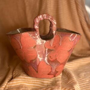 Håndbygget keramikkvase formet som en veske med blomsterdekor og glaserte farger.