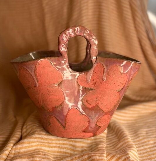 Håndbygget keramikkvase formet som en veske med blomsterdekor og glaserte farger.