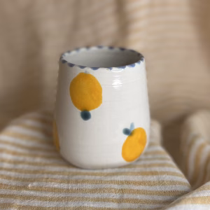 Liten håndlaget kopp med håndmalt appelsinmotiv på lys keramikk. SEO