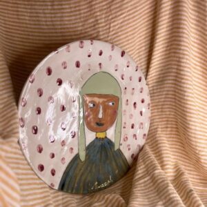 Håndmalt rundt keramikkfat med naivistisk portrettmotiv og røde prikker på lys bakgrunn, laget av Caroline Sagafos på Bekkelund Gård & Keramikk.