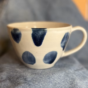 Håndlaget tekopp med blå håndmalte dotter på lys keramikk.