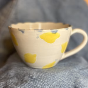 Håndlaget tekopp med gult sitronmotiv og blå detaljer på lys keramikk.