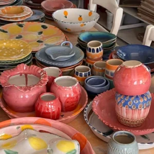 Håndlagde keramikkfat, kopper og boller i fargerike glasurer stående samlet på verkstedet hos Bekkelund Gård & Keramikk.